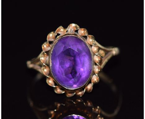 A 9ct gold ring set with an oval cut amethyst with a twisted border, 1.9g, size K
