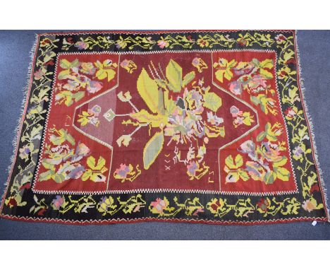A large rug with central abstract yellow motif on a wine ground, within a black border and floral surround, 310 x 220cm