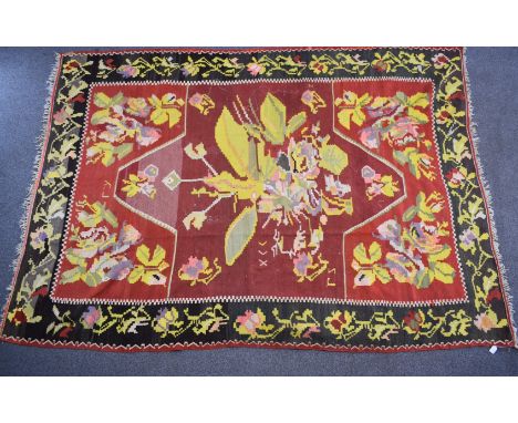 A large rug with central abstract yellow motif on a wine ground, within a black border and floral surround, 310 x 220cm