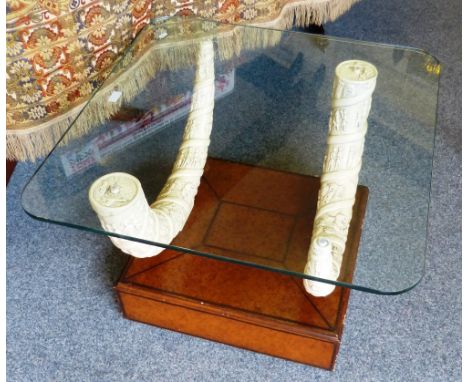 A contemporary glass topped sofa table, composed of two resin 'carved ivory tusks' supporting a toughened glass top