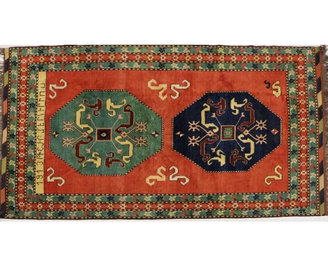 A large Caucasian style rug, late 20th century, with two large blue and green medallions to a red field, enclosed by a green 