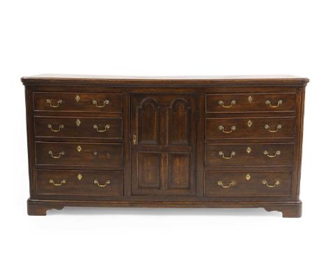 A George III oak dresser base late 18th century, the rounded rectangular top above a central arcaded cupboard, flanked by sho