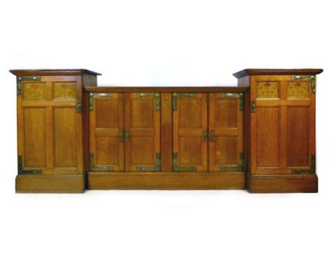 An Arts & Crafts oak, marquetry, and brass mounted sideboard, the central section with two pairs of paneled cupboard doors, f