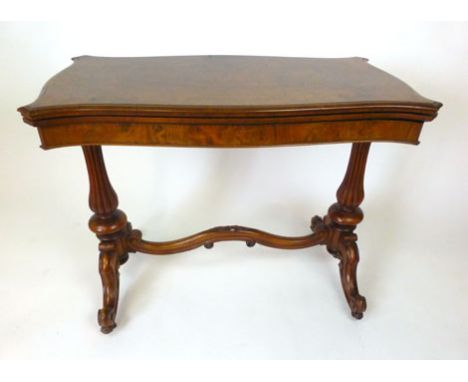 A Victorian burr walnut card table, the fold over serpentine shaped top on reeded end supports joined by a carved serpentine 