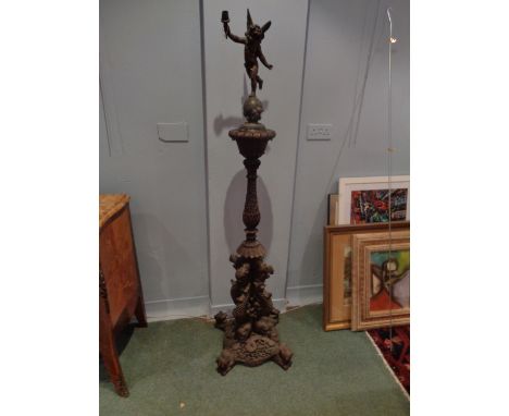 A Teak carved Burmese Standard Lamp with a figure of Eros on a globe holding a lamp.