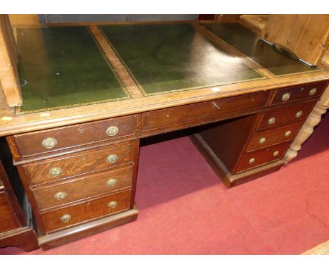 A late Victorian oak and gilt tooled green leather inset twin pedestal writing desk, having an arrangement of nine drawers wi