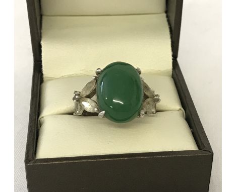 A silver dress ring set with oval jade cabochon, and clear stones in flower design to shoulders. Ring size N½. 