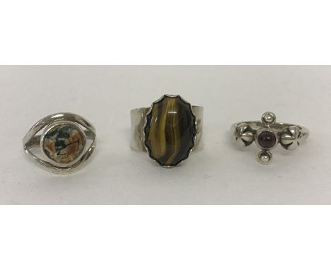 3 silver stone set dress rings. An oval tigers eye adjustable ring, a floral design with central small garnet cabochon and a 