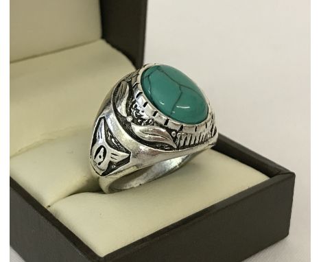 A large white metal dress ring with carved detail and set with oval shaped piece of turquoise.  Ring size T.