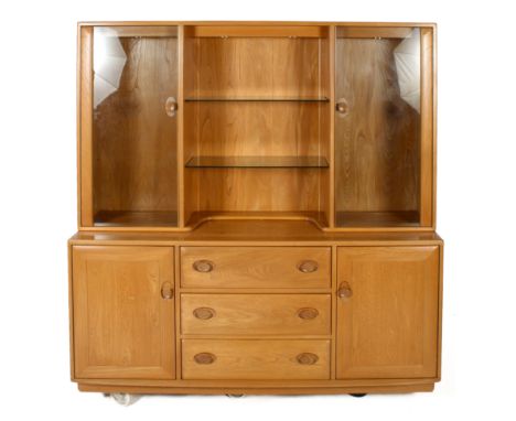 An Ercol two-part cabinet. With two glazed cupboards flanking glass shelves to the top, over three drawers and two cupboards.