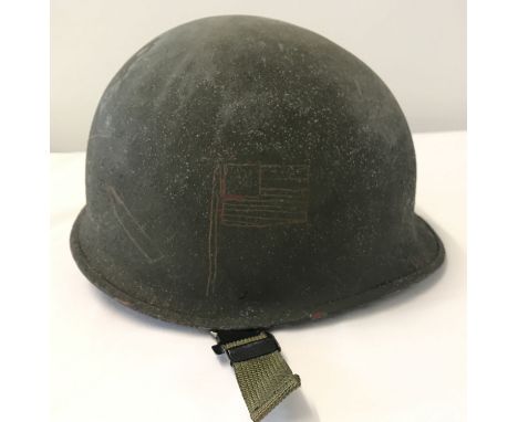 A US army M1 steel helmet with trench art detail, complete with liner. US flag, bomb, bullet and cats eyes all scratched into