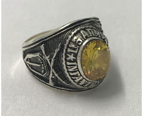 A Vietnam war style white metal Army class ring with central yellow stone.  Ring size X.