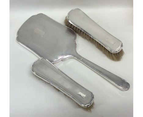 An engine turned silver dressing table mirror together with two matching brushes. Birmingham. Approx. 332 grams. Est. £25 - £