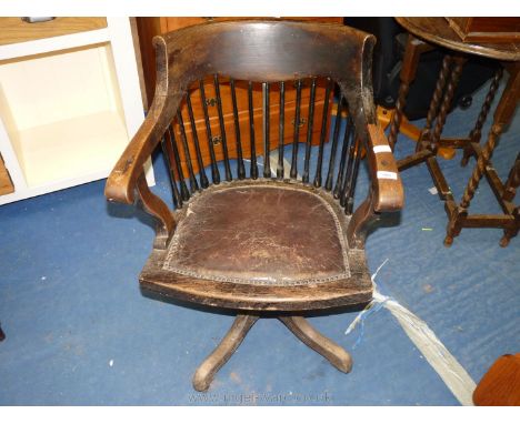 An oak leather seated stick back swivel captains chair with metal swivel mechanism.