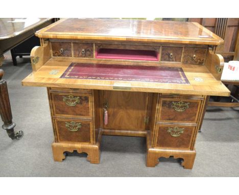 A reproduction walnut veneered knee hole desk in the Georgian style, the fitted top secretaire drawer with a red leather writ