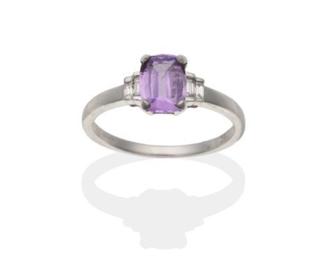 An 18 Carat White Gold Purple Sapphire and Diamond Ring, an oval cut purple sapphire in a claw setting, spaced by graduated b