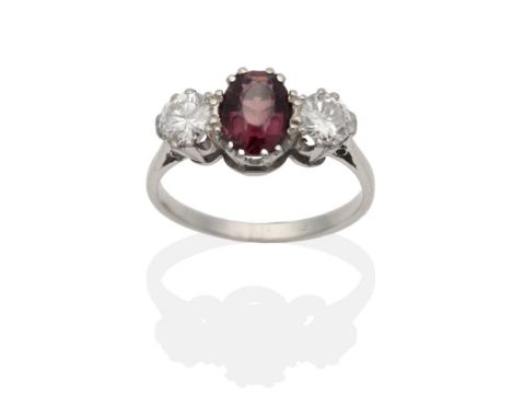 A Garnet and Diamond Three Stone Ring, an oval cut garnet between round brilliant cut diamonds in claw settings, to knife edg