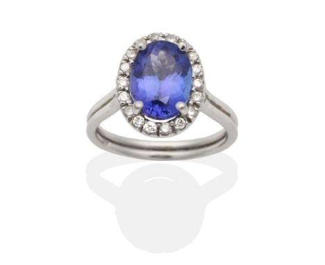 A Tanzanite and Diamond Cluster Ring, an oval cut tanzanite in a claw setting, within a border of round brilliant cut diamond