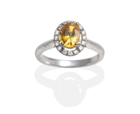 An 18 Carat White Gold Yellow Sapphire and Diamond Cluster Ring, an oval cut yellow sapphire in a claw setting within a diamo