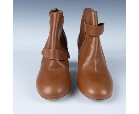 New tan leather ankle boots feature a sleek and minimal design with a side zipper closure for easy wear. A strap detail with 