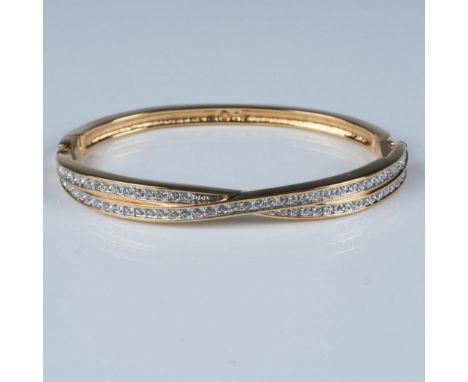 An exquisite gold-tone plated hinged bangle bracelet, adorned with rows of clear crystals that cross at the center. Swarovski