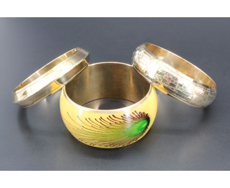 Two brass bangles, one decorated with a woven brass and copper lattice, together with a brass bangle having a hand painted pe