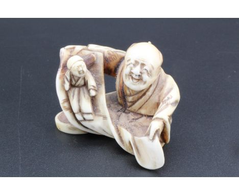 A Japanese ivory netsuke of a man opening a scroll with a child inside, 4 cm