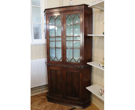 A late Georgian mahogany standing corner cabinet, having a pair of glazed doors enclosing three shaped shelves and a painted 