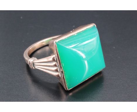 A vintage jade finger ring, comprising a square cabochon bezel-set on an Art Deco influenced yellow metal shank with tapering