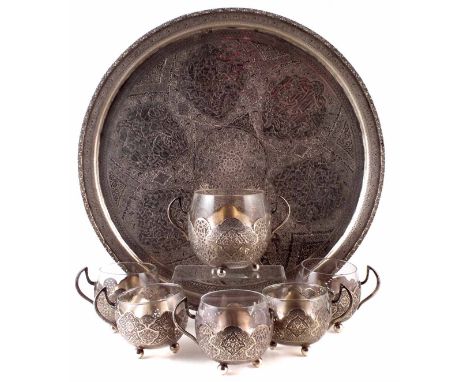 A Turkish circular silver tray, decorated with intricate floral designs and scrollwork, inset with various scenes depicting w