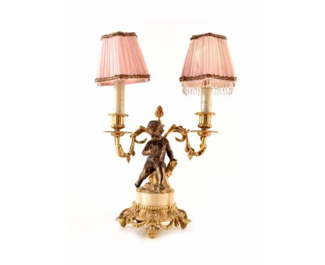 A twin branched table lamp in an ormolu style with gilded detail surrounding a central cherub holding fruit. With two beaded 