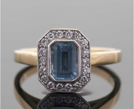 An 18ct aquamarine and diamond ring, the central emerald cut aquamarine in rubover mount, surrounded by round brilliant cut d