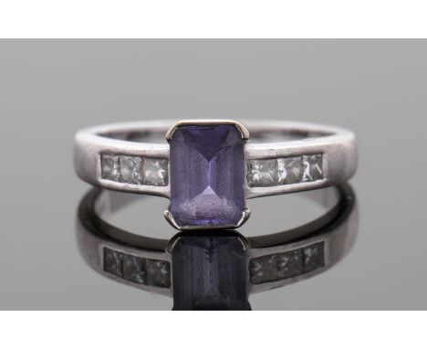An 18ct white gold tanzanite and diamond ring, the central emerald cut tanzanite in half rubover mount, 7.1mm long, with prin