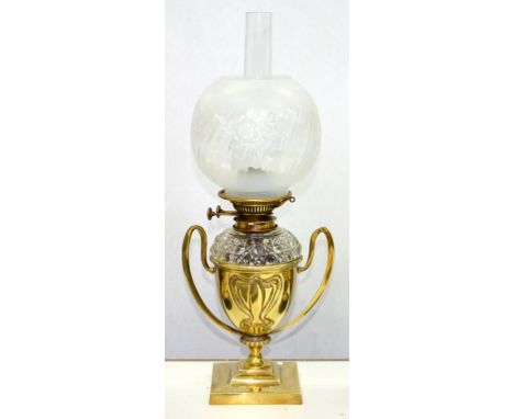 AN EDWARD VII EMBOSSED BRASS TWO HANDLED SHIELD SHAPED OIL LAMP, ON SQUARE FOOT WITH DETACHABLE CUT GLASS SHOULDER FOUNT AND 