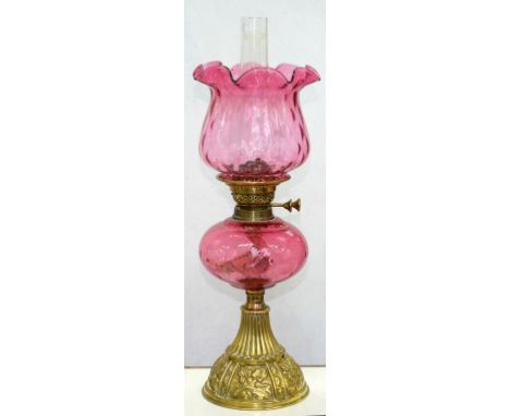 AN EDWARD VII EMBOSSED BRASS COVERED OIL LAMP OF DOMED SHAPE WITH PANELS OF IVY LEAVES AND CRANBERRY GLASS FOUNT, BRASS BURNE