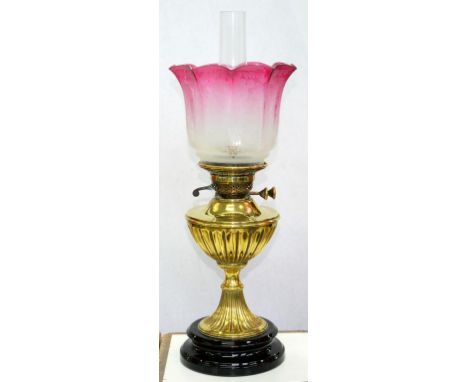 A VICTORIAN EMBOSSED BRASS TRUMPET SHAPED OIL LAMP, WITH BRASS FOUNT AND BURNER ON BLACK GLAZED POTTERY FOOT WITH ETCHED AND 