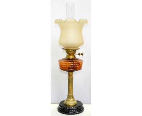 A VICTORIAN REEDED BRASS COLUMNAR OIL LAMP, WITH AMBER GLASS FOUNT, BRASS BURNER AND BLACK GLAZED POTTERY FOOT WITH A FROSTED