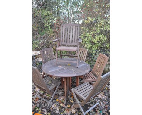 A STAINED TEAK CIRCULAR GATE LEG GARDEN TABLE, diameter 120cm x height 77cm, and six folding chairs including two carvers (co