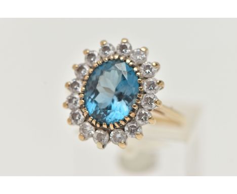 A 9CT GOLD CLUSTER RING, centring on an oval cut blue topaz, in a surround of colourless cubic zirconia, open work gallery, p