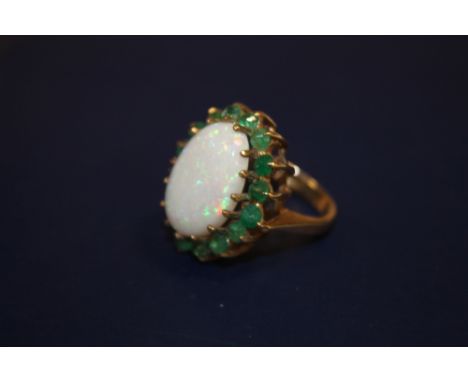 A BOXED 9CT GOLD DRESS RING SET WITH A LARGE OPAL SURROUNDED BY SMALL EMERALDS 