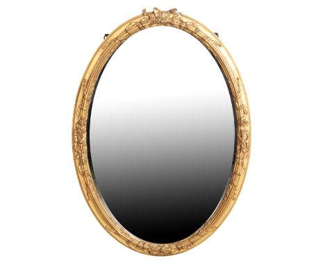 A GILTWOOD AND COMPOSITION FRAMED OVAL WALL MIRROR, late 19th century, with foliate cresting and ribbon work in relief to sid