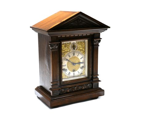 An early 20th Century walnut cased bracket clock in architectural form with carved corinthian pillars supporting a triangular