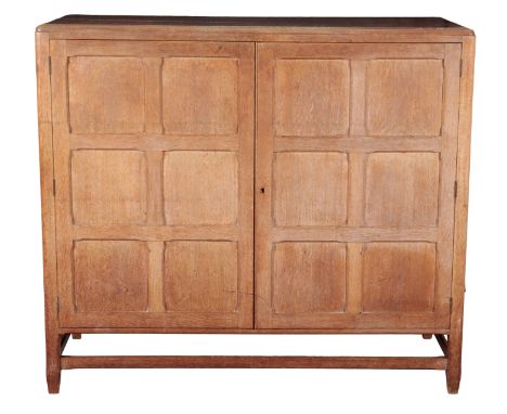 A COTSWOLD SCHOOL STYLE OAK TWO-DOOR PANELLED CABINET the doors with chamfered lattice-work panelling, opening to reveal a va