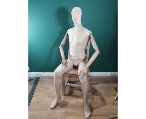 A seated male Shop Mannequin with fabric covered head, torso and legs and wooden arms, with swivelling lower torso and articu
