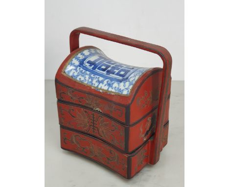 A Chinese three tier lacquered Tiffin Carrier, the lid with inset blue and white tile, with red lacquer and gilt floral desig