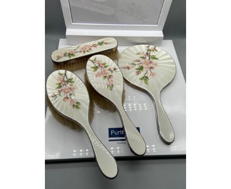 A Four piece London silver and enamel floral design dressing table set. The set consists of a hand mirror and three brushes. 