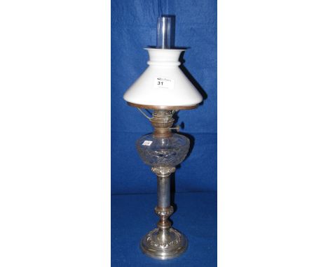 Small silver plated oil lamp with moulded clear glass reservoir and white shade with glass chimney.
