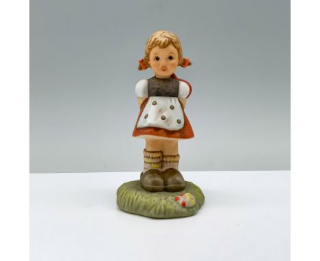 In her red, white, and gray schoolgirl outfit, a young girl stands atop a field of grass, her hands tucked behind her back wi
