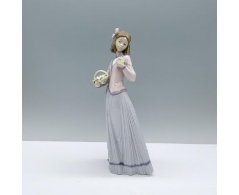 A young woman in a pink sweater and long lavender skirt holding a basket of flowers while admiring a few from the set. Lladro