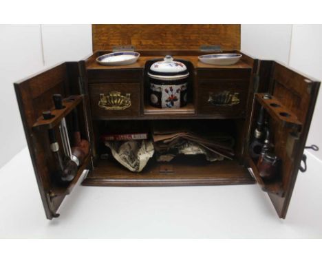 AN EDWARDIAN OAK SMOKER'S CABINET, hinged lid and two doors to front, fitted brass side carrying handles, opening to reveal a